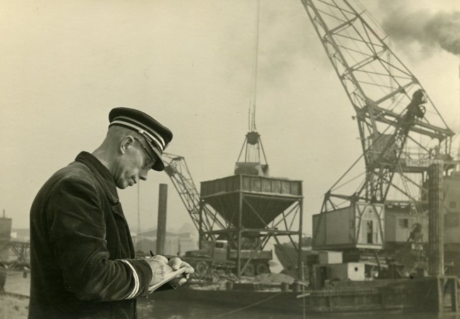 Een ambtenaar van de Provinciale Waterstaat controleert een zandtransport. Dit zand wordt gebruikt voor de aanleg van wegen en dijken. De foto is vermoedelijk gemaakt tussen 1950 en 1960.