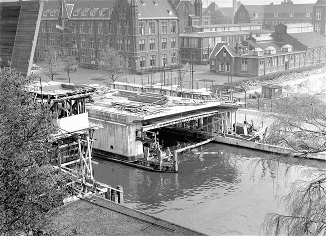 Overzicht van de bouw van de eerste St. Sebastiaansbrug over het Rijn-Schiekanaal. Op de achtergrond het voormalige laboratorium van de Afdeling Physica en Electrotechniek van de Polytechnische School.