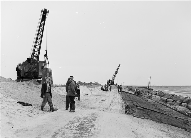 Dijkherstel bij Oude-Tonge na de watersnoodramp van 1 februari 1953. Met behulp van draglines wordt een nieuw dijklichaam gevormd. Een gedeelte van de dijk is al bekleed met zandasfalt.