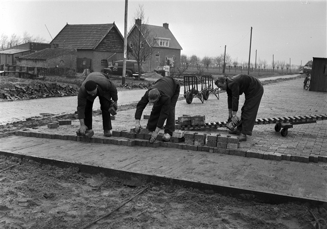Aanleg van de (drijvende) weg nr. 29 tussen Gouda, Stolwijk en Bergstoepseveer. Stratenmakers bestraten de weg met betonklinkers (ipro H-profiel keien).