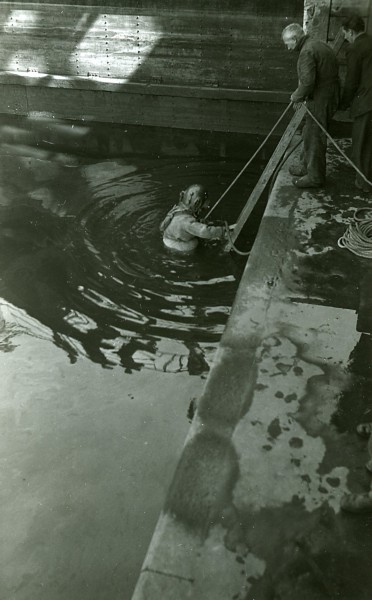 Een duiker voert waarschijnlijk een onderwaterinspectie uit bij een brug of een sluis. De foto is gemaakt tussen 1920 en 1940.