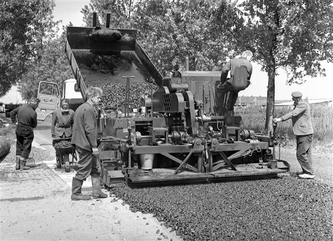 Verbetering van de Tiendweg. Met een Barber-Greene asfaltmachine wordt op de fundering van gewalst puin een deklaag aangebracht van grof asfaltbeton.