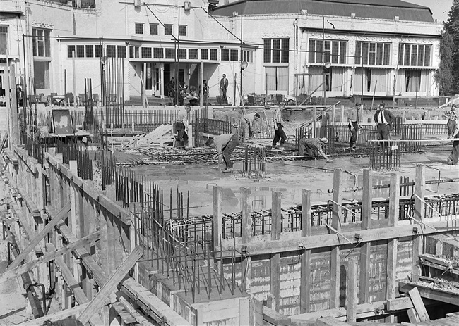 Betontimmermannen strijken het beton uit van de souterrainvloer, van het nieuwe provinciehuis. Op de achtergrond het restaurant van de voormalige Haagsche Dierentuin, dat in 1968 is gesloopt.