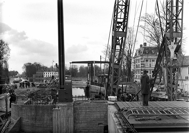 Een drijvende bok plaatst de onderdelen van de in aanbouw zijnde Oude Tolbrug over het Rijn-Schiekanaal, beter bekend als de Vliet. Op de achtergrond de voormalige Oude Tolbrug die later wordt gesloopt.