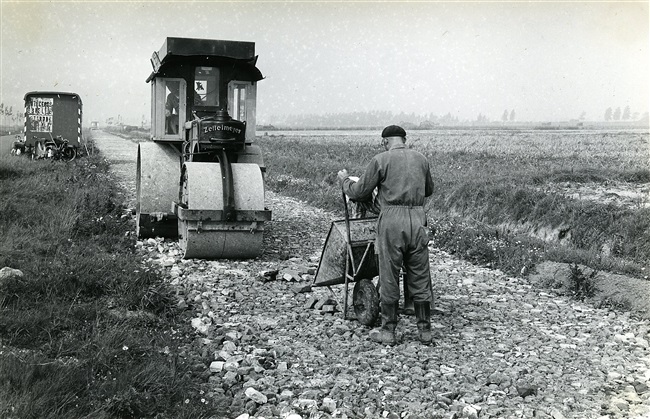 Een Zettelmeyer wals wordt gebruikt bij de aanleg van de provinciale weg nr. 47. Een laag puin wordt ingewalst en volgespoten met leemgrond en daarna ingewassen.