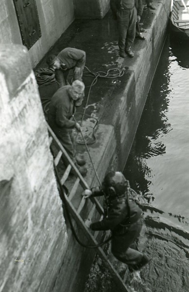 Een duiker voert waarschijnlijk een onderwaterinspectie uit bij een brug of een sluis. De foto is gemaakt tussen 1920 en 1940.