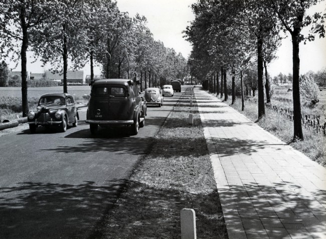 Een nieuw aangelegde weg door de Provinciale Waterstaat. Op de voorgrond rechts rijdt een dienstauto van de gemeente Rotterdam. De foto is waarschijnlijk gemaakt tussen 1950 en 1959.