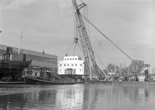 Een sleepboot van N.V. Reederij v/h Gebr. Goedkoop versleept een coaster die te water is gelaten.