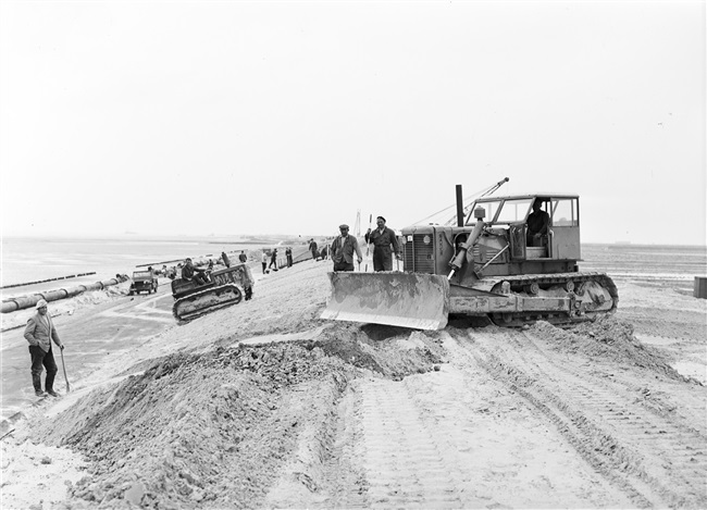 Dijkherstel bij Oude-Tonge na de watersnoodramp van 1 februari 1953. Het profiel van het nieuwe dijklichaam wordt met machines aangepast (geprofileerd).