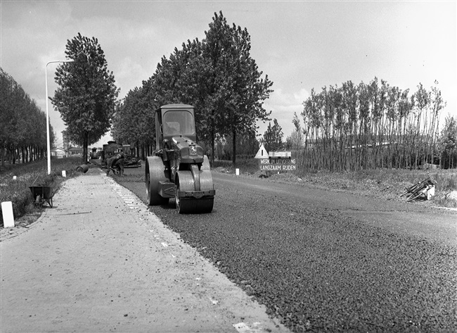 Een walsmachinist verdicht het asfalt met een wals, bij de verbetering van de Tiendweg.