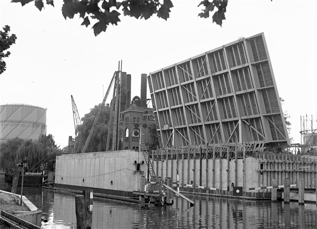 Overzicht van de remmingpalen bij de bouw van de eerste St. Sebastiaansbrug. De basculebrug over het Rijn-Schiekanaal verbindt de oude binnenstad van Delft met de TU-wijk. Op de achtergrond de gasfabriek, die later is gesloopt.
