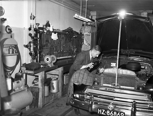 Een monteur kijkt een dienstauto na. Deze garage van de provincie Zuid-Holland is aan de Billitonstraat 10A in Den Haag. De foto is waarschijnlijk gemaakt tussen 1950 en 1964.