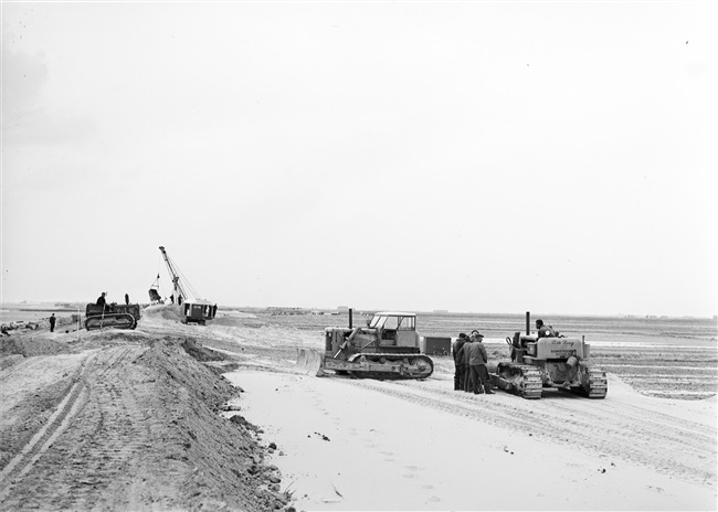 Dijkherstel bij Oude-Tonge na de watersnoodramp van 1 februari 1953. Met behulp van machines en draglines wordt een nieuw dijklichaam gevormd.