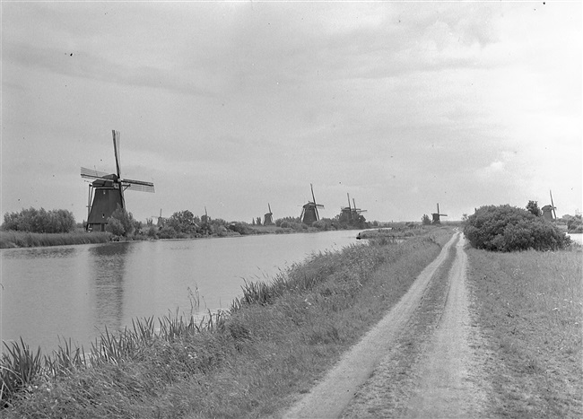 Onverharde weg waar fietspad nr. 19 komt. Door het aanleggen van fietspaden ontsluit de provincie Zuid-Holland poldergebieden voor recreatie. Links de molens van Kinderdijk.