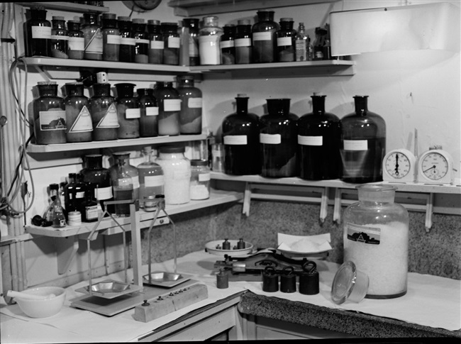 De Fotografische afdeling van de Provinciale Waterstaat. In de donkere kamer (doka) staan een weegschaal en chemicaliën voor het ontwikkelen en afdrukken van foto’s. Deze foto is gemaakt rond 1960.