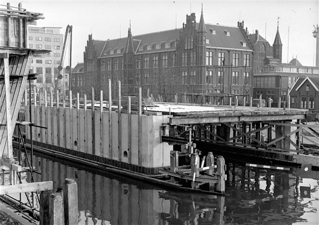 Bouw van de vaste overspanning van de eerste St. Sebastiaansbrug over het Rijn-Schiekanaal. Op de achtergrond het voormalige laboratorium van de Afdeling Physica en Electrotechniek van de Polytechnische School.