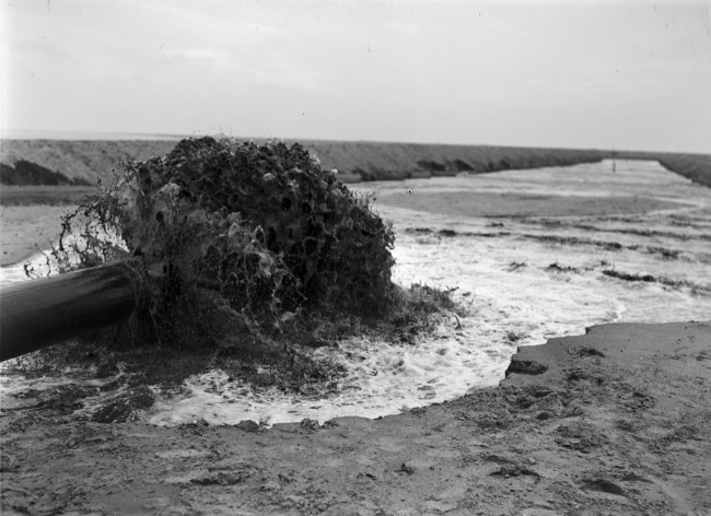 De dijk bij Stellendam wordt hersteld na de watersnoodramp van 1 februari 1953. Zand en water worden via een buis geperst naar de plek waar een nieuw dijklichaam wordt opgespoten.