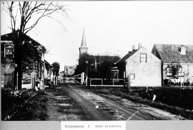 De tol in Kwintsheul. De Kerkstraat, de vroegere Broekweg, is afgesloten met een tolboom. Met de inkomsten van tolwegen werden wegen aangelegd en onderhouden. De foto is gemaakt tussen 1930 en 1949.