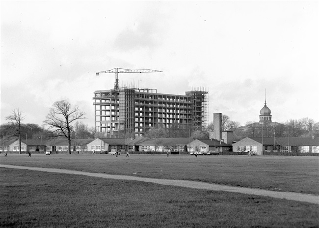 Het betonskelet van de hoogbouw van het nieuwe provinciehuis, gezien vanaf het Malieveld. Rechts het Moorse Paleis van de voormalige Haagsche Dierentuin. Op de voorgrond vermoedelijk de noodgebouwen van Rijkswaterstaat.