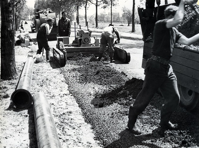 Asfaltwerkers repareren het wegdek met koudasfalt oftewel reparatieasfalt. De foto is waarschijnlijk gemaakt tussen 1960 en 1969.