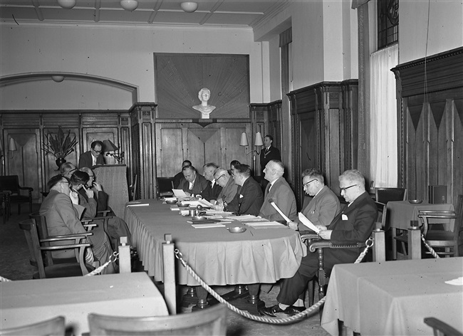 Openbare vergadering van Gedeputeerde Staten in Den Haag. Aan tafel zitten van achteren naar voren gezien: gedeputeerden Harm van Riel, T.A. van Dijken, A.C.A. Deerenberg, commissaris van de Koningin Jan Klaasesz, griffier F.A. Helmstrijd, gedeputeerden J.P. van Praag en D. van der Kwaak.