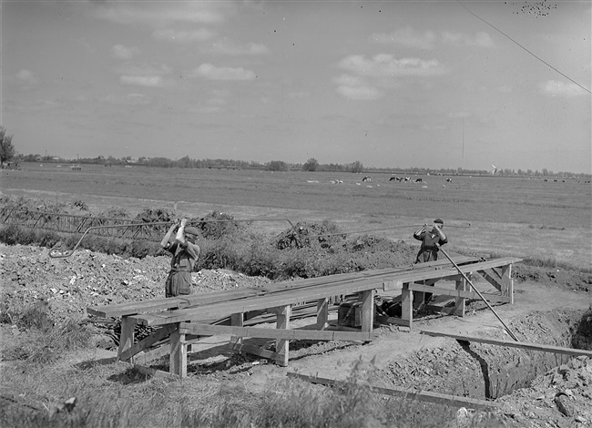 Aanleg van de weg op palen tussen Boskoop en Alphen aan den Rijn. IJzervlechters buigen het ijzer voor de wapening van de dwarsbalken. Op de dwarsbalken komt later het wegdek te rusten.