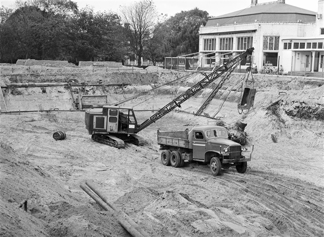 Met een dragline wordt een boomstronk verwijderd, voor de bouw van het nieuwe provinciehuis. Rechts het restaurant van de voormalige Haagsche Dierentuin, dat in 1968 is gesloopt.