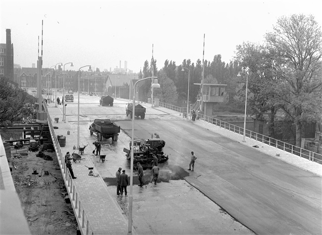 Asfaltwerkers brengen de asfalt wegverharding aan op de eerste St. Sebastiaansbrug. De basculebrug over het Rijn-Schiekanaal verbindt de oude binnenstad van Delft met de TU-wijk.