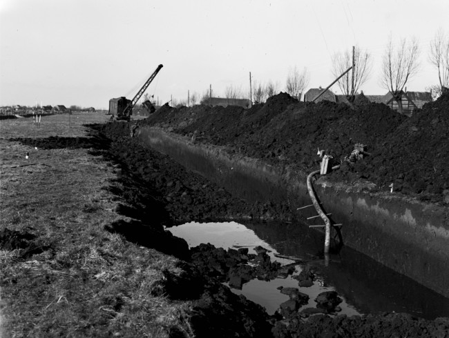 Aanleg van de provinciale weg nr. 29 tussen Gouda en Stolwijk. Met een dragline wordt een cunet, dat is een brede sleuf, gegraven. Daarin komt een laag houtvezelbalen met daarop een rijzenbed constructie, een laag zand en een wegverharding van ipro H-profiel keien.