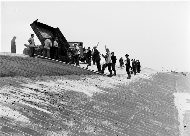 Dijkherstel bij Oude-Tonge na de watersnoodramp van 1 februari 1953. Het nieuwe dijklichaam van opgespoten zand wordt bekleed met zandasfalt.