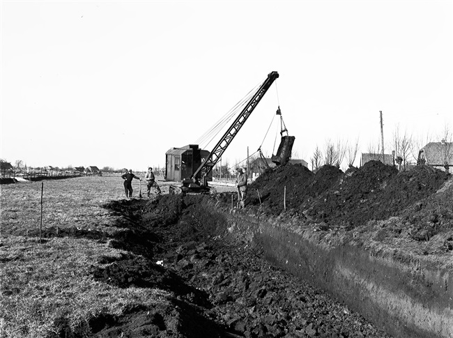 Aanleg van de provinciale weg nr. 29 tussen Gouda en Stolwijk. Met een dragline wordt een cunet, dat is een brede sleuf, gegraven. Daarin komt een laag houtvezelbalen met daarop een rijzenbed constructie, een laag zand en een wegverharding van ipro H-profiel keien.