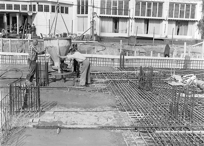 Betonstorters storten met een betonkubel de souterrainvloer van het nieuwe provinciehuis. Op de achtergrond het restaurant van de voormalige Haagsche Dierentuin, dat in 1968 is gesloopt.