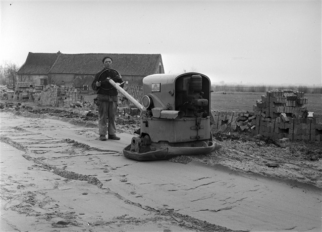 Aanleg van de (drijvende) weg nr. 29 tussen Gouda, Stolwijk en Bergstoepseveer. Een man verdicht het zand en maakt het vlak met een handgevoerde trilwals.