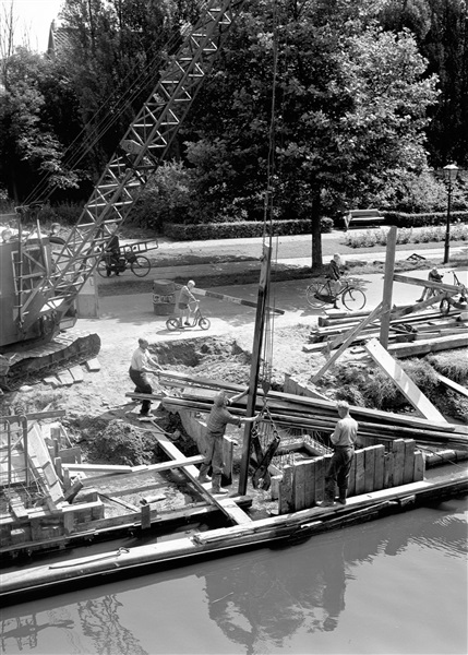 Een houten damwand wordt getrokken bij de bouw van de eerste St. Sebastiaansbrug over het Rijn-Schiekanaal.