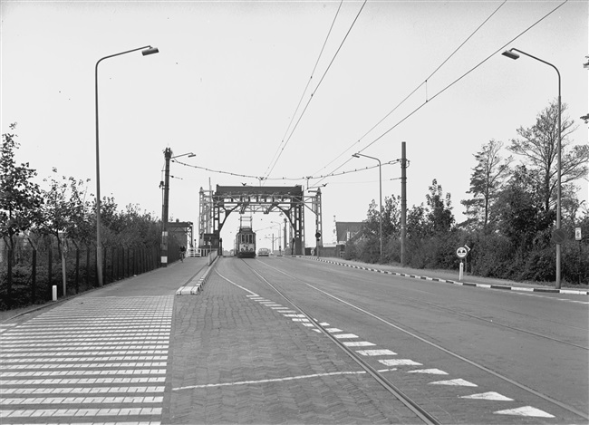 De Haagse Schouwbrug over de Oude Rijn. De tram komt uit Den Haag en rijdt richting Leiden. De tramdienst werd 9 november 1961 opgeheven. Rechts van de brugportalen de nog bestaande witte trapgevel van het restaurant Haagse Schouw, van de familie Van der Valk.