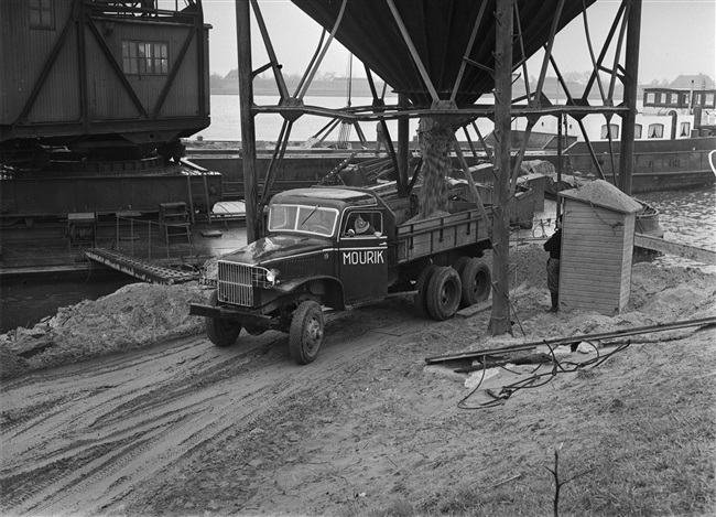 Schip laadt zand over in zandauto voor aanleg S29/N207, 1956
