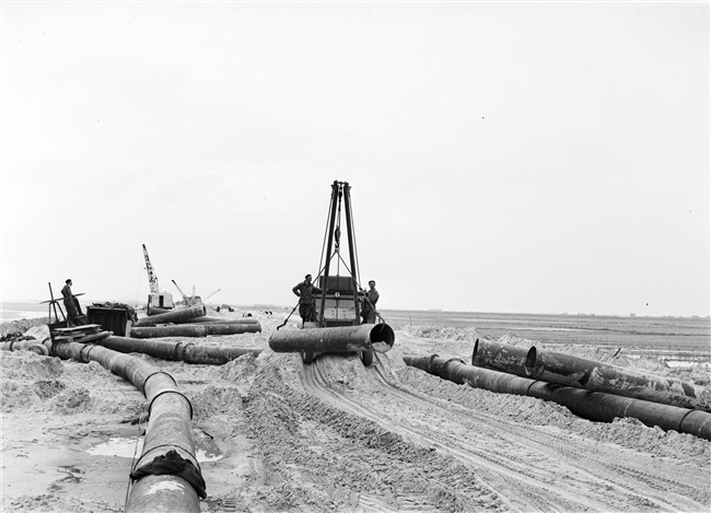 De dijk bij Oude-Tonge wordt hersteld na de watersnoodramp van 1 februari 1953. Zand en water worden via een buis geperst naar de plek waar een nieuw dijklichaam wordt opgespoten.