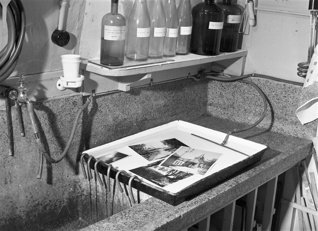 De donkere kamer (doka) van de Fotografische afdeling van de Provinciale Waterstaat aan de Riouwstraat. Afgedrukte foto's worden in een ontwikkelbak met water gespoeld. Deze foto is gemaakt rond 1960.