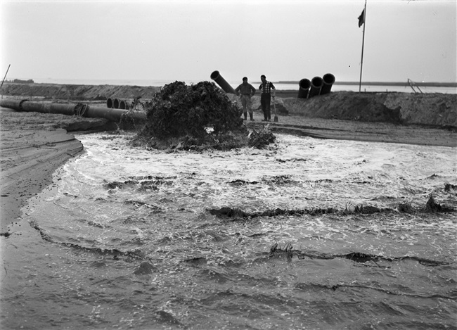 De dijk bij Stellendam wordt hersteld na de watersnoodramp van 1 februari 1953. Zand en water worden via een buis geperst naar de plek waar een nieuw dijklichaam wordt opgespoten.