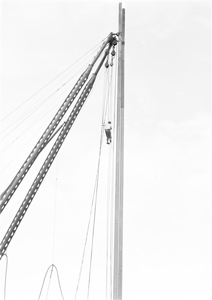 Aanleg van de weg op palen tussen Boskoop en Alphen aan den Rijn. Een man hangt in een heistelling om kabels te ontwarren.