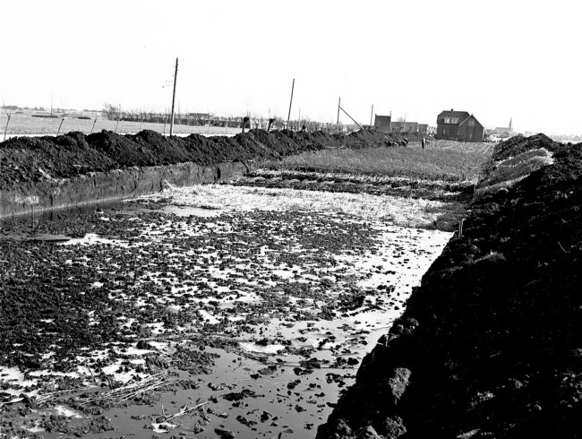 Aanleg van de provinciale weg nr. 29 tussen Gouda en Stolwijk. Om de draagkracht van de bodem te vergroten is een cunet, dat is een brede sleuf, gegraven. Daarin komt een laag houtvezelbalen met daarop een rijzenbed constructie, een laag zand en een wegverharding van ipro H-profiel keien.